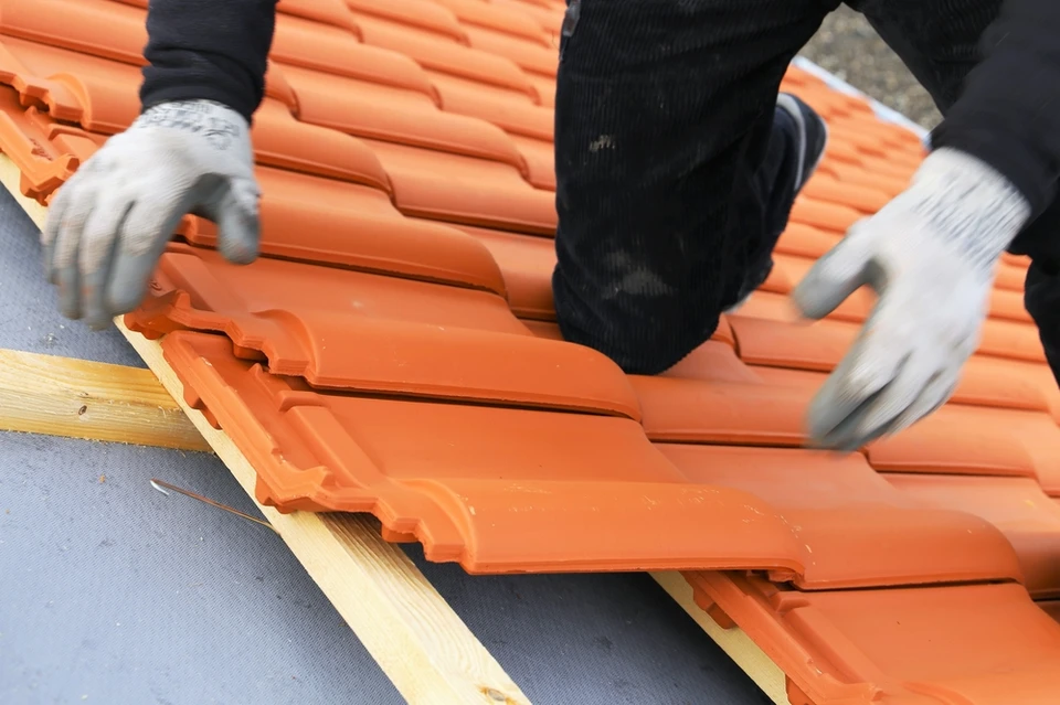 Chantier extérieur de couverture avec ouvrier posant des tuiles terre cuite orange sur charpente bois