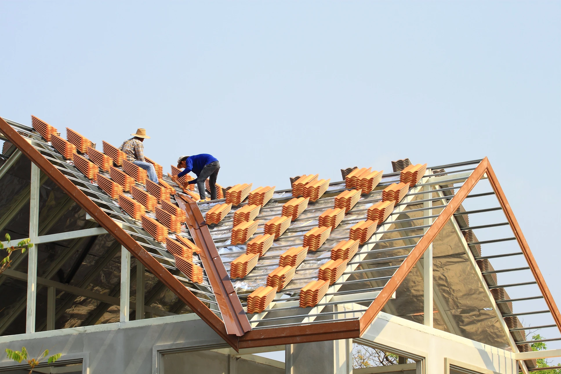 Chantier de construction extérieur avec ouvriers installant des tuiles terre cuite sur toiture en pente