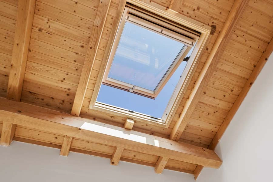 Pièce mansardée vide avec grande fenêtre panoramique donnant sur jardin arboré